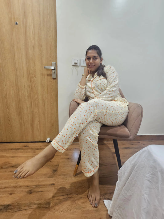 Woman in a floral pajama set sitting on a chair in a room with wooden floor and white wall.