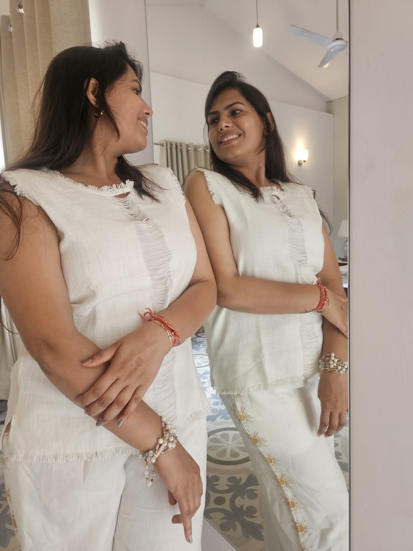 Woman in a white outfit standing in front of a mirror, wearing jewelry.